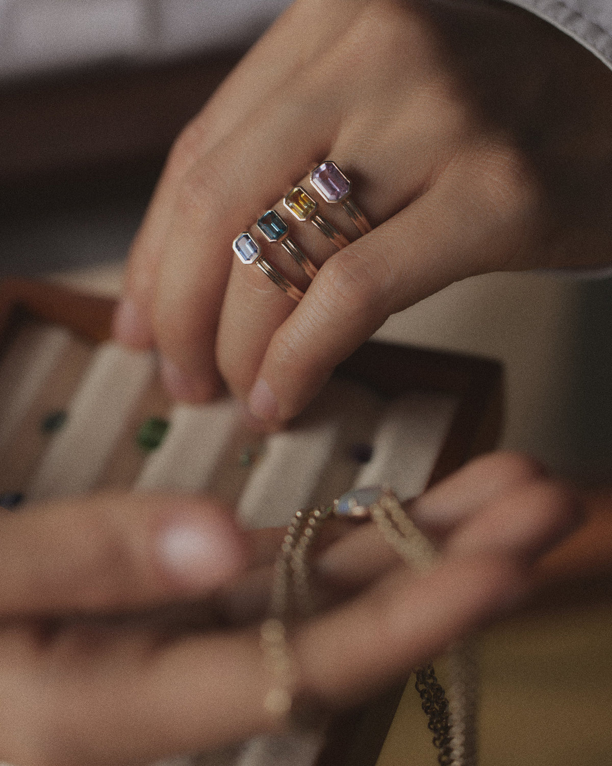 [lifestyle]Close-up of hands wearing rings with colorful gemstones on a neutral background