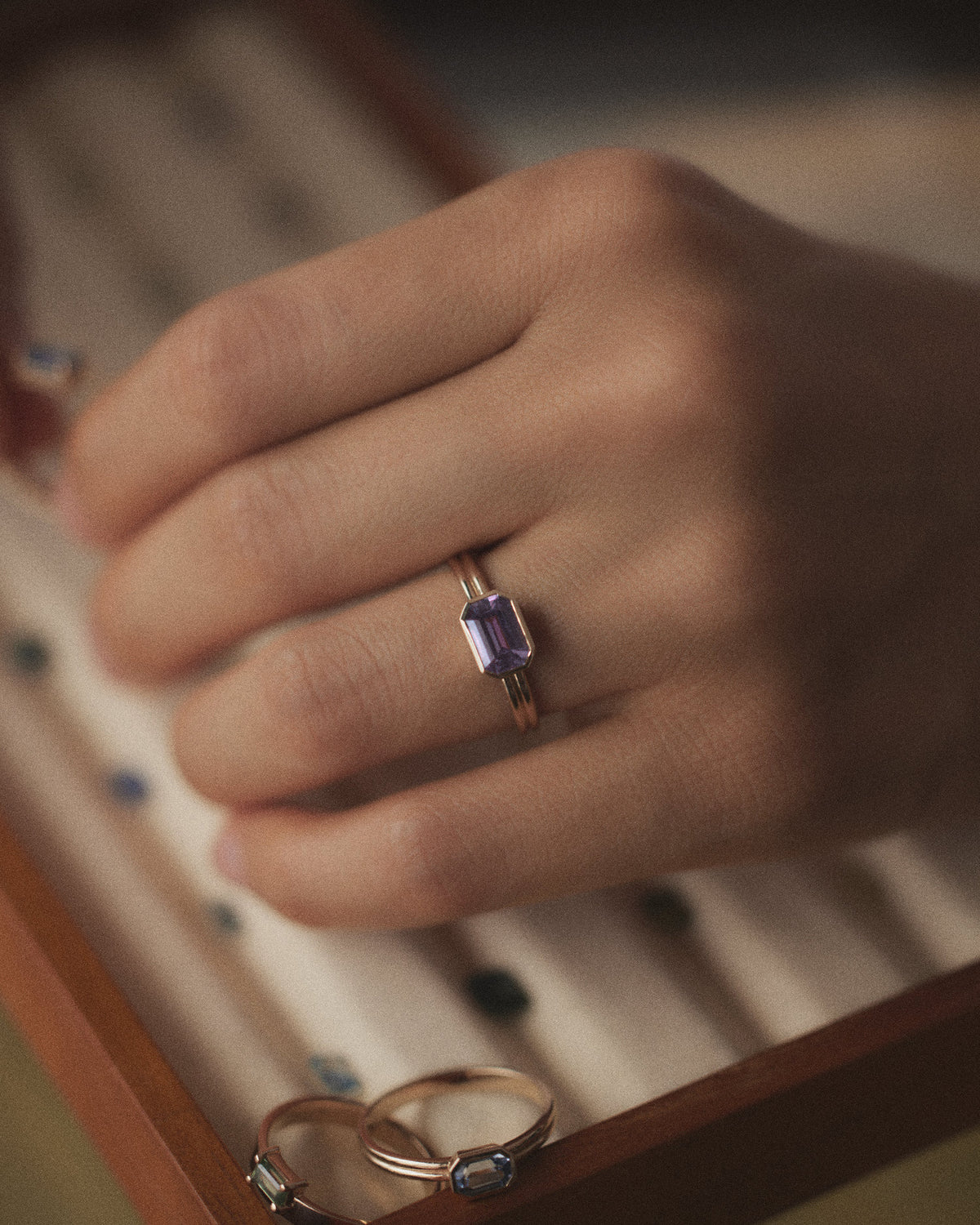 [lifestyle]Hand wearing a gold ring with a purple gemstone in a jewelry box.