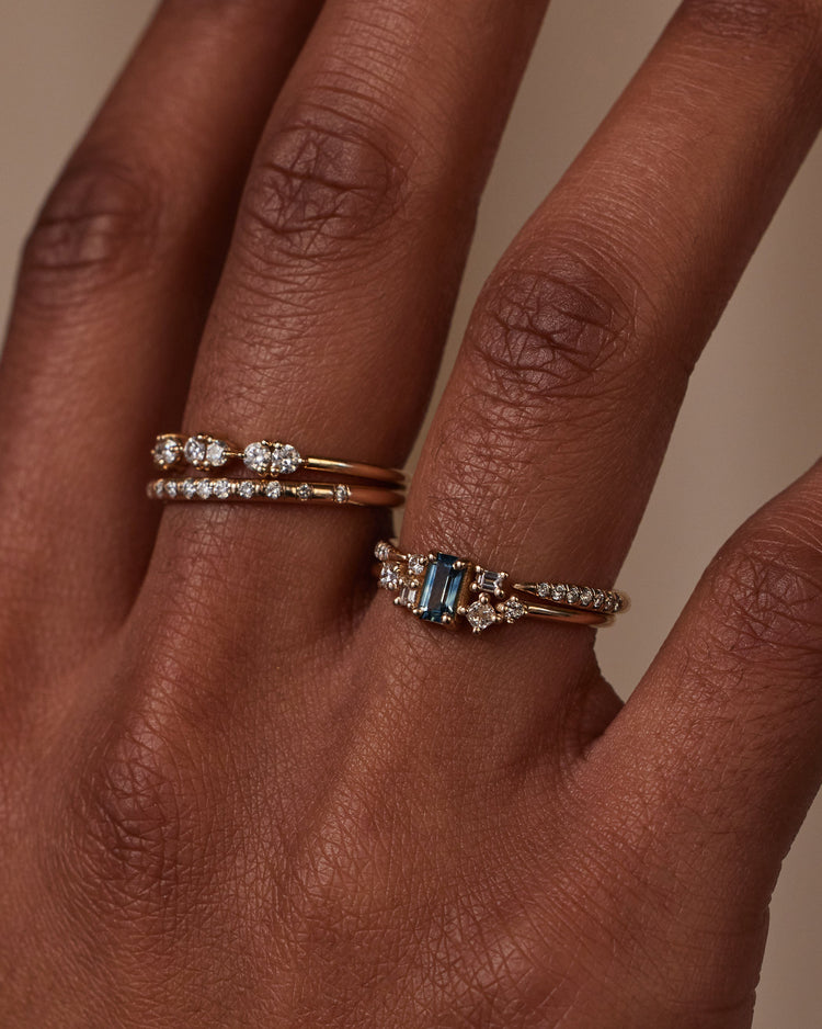 [lifestyle]Close-up of a hand wearing two gold rings with gemstones on a neutral background