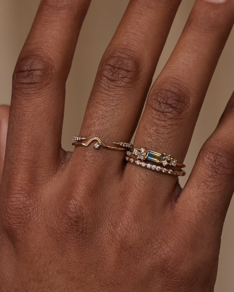 [lifestyle]Hand wearing two gold rings with gemstones on a neutral background