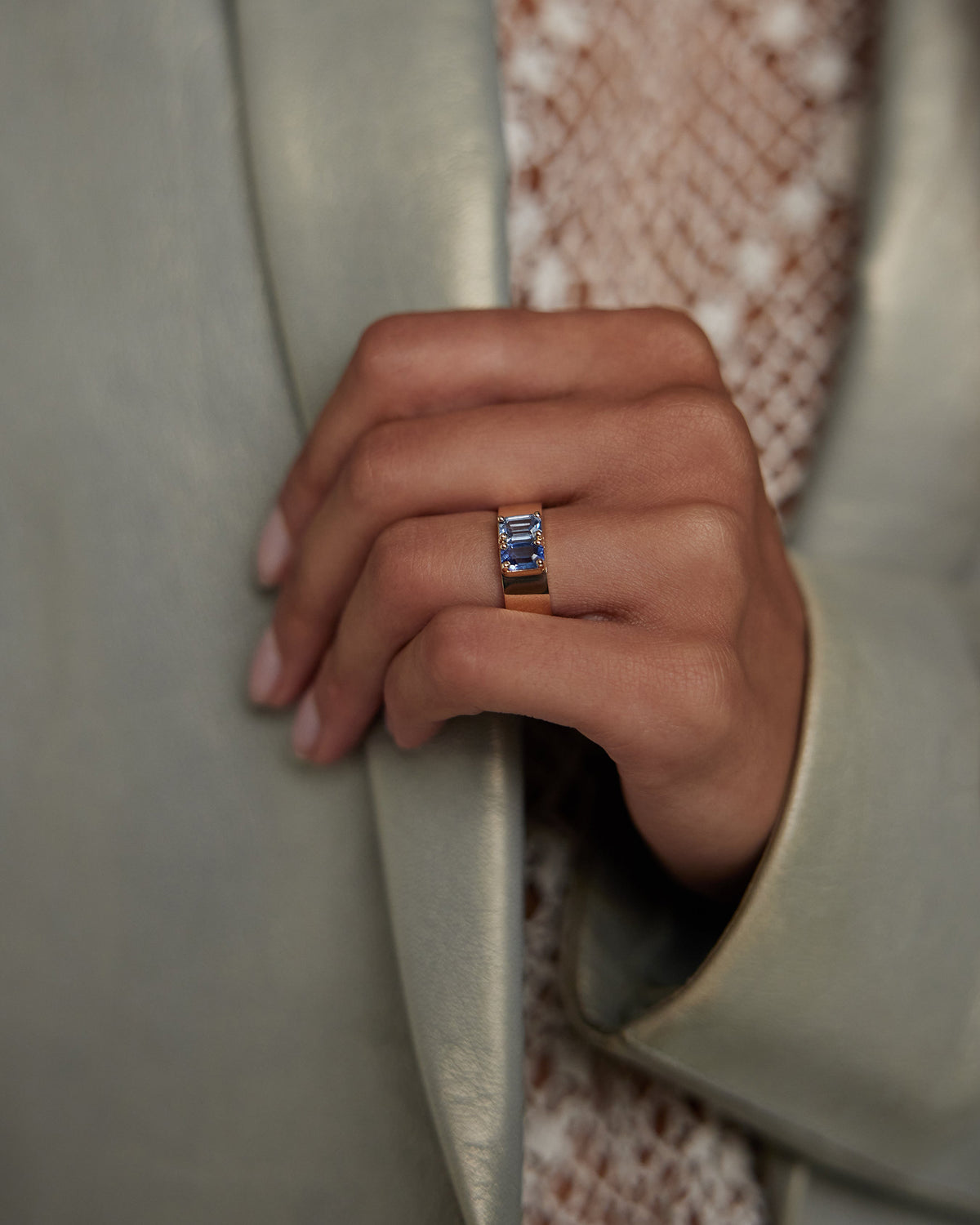 [lifestyle]Close-up of a hand wearing a ring with a blue gemstone, set against a neutral background.