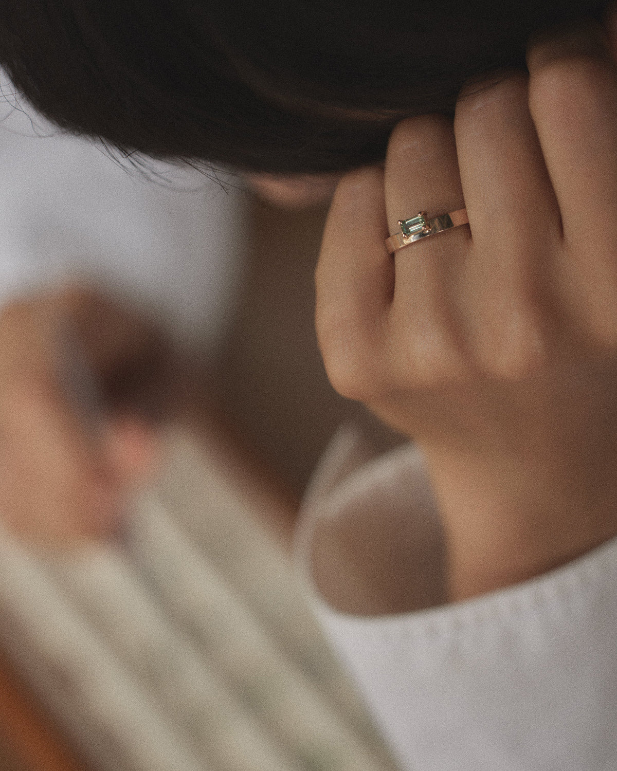 [lifestyle]Close-up of a hand wearing a ring with a green gemstone, blurred background