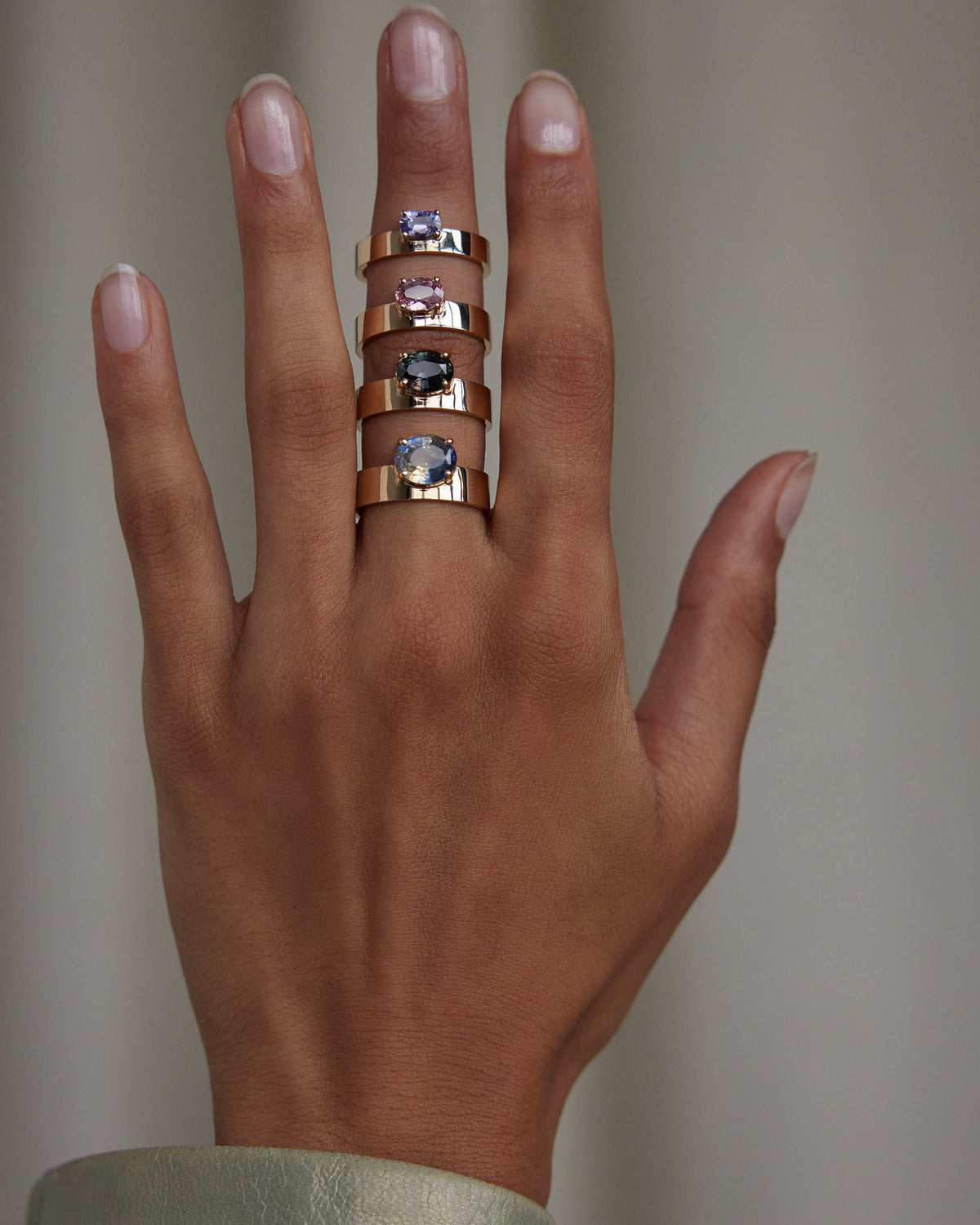 [lifestyle]Hand wearing multiple rings with gemstones on a neutral background
