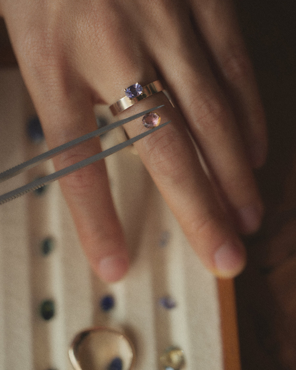 [lifestyle]Close-up of a hand wearing a ring with a purple gemstone on a neutral background