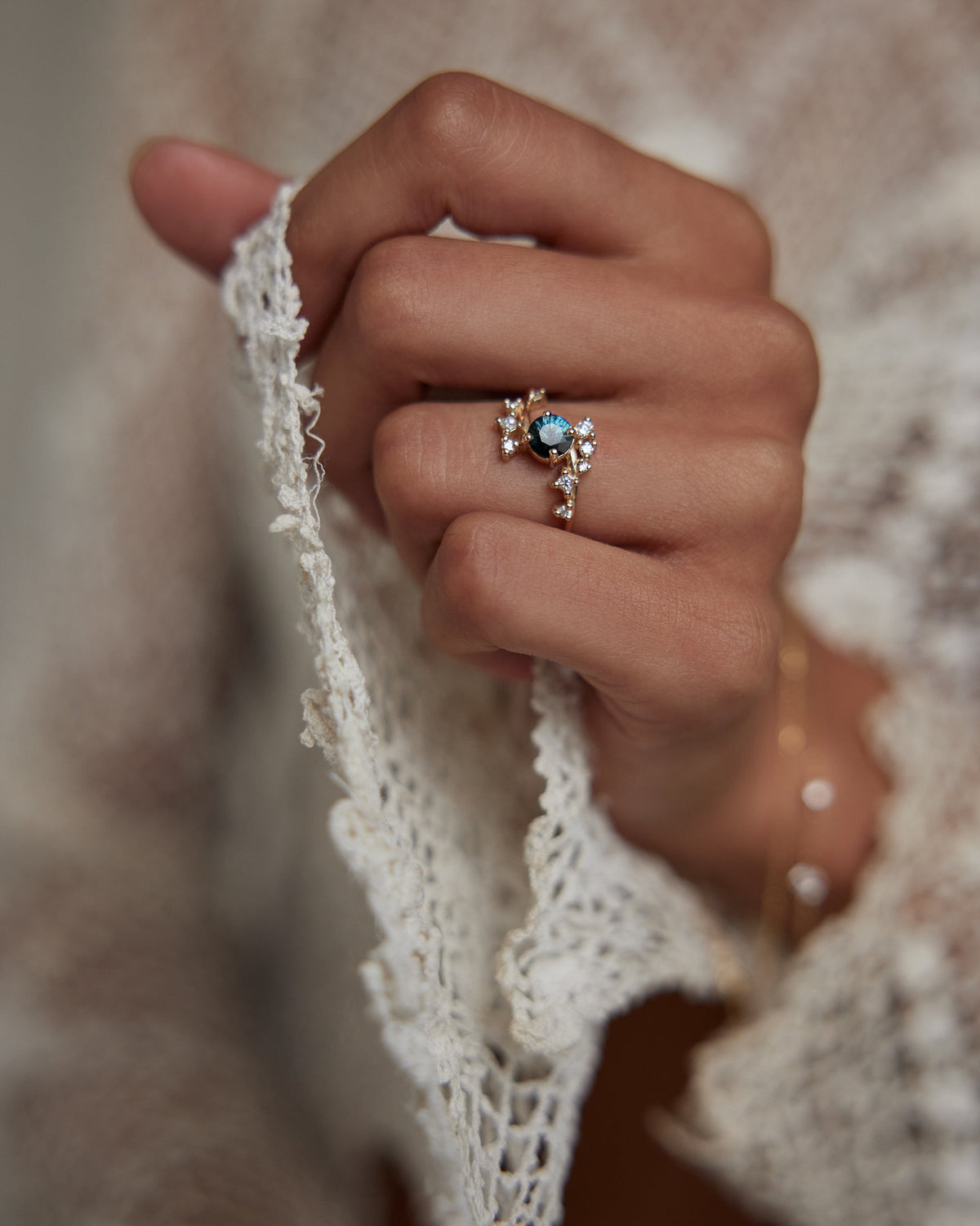 [lifestyle]Close-up of a hand wearing a ring with a blue gemstone on a textured fabric background