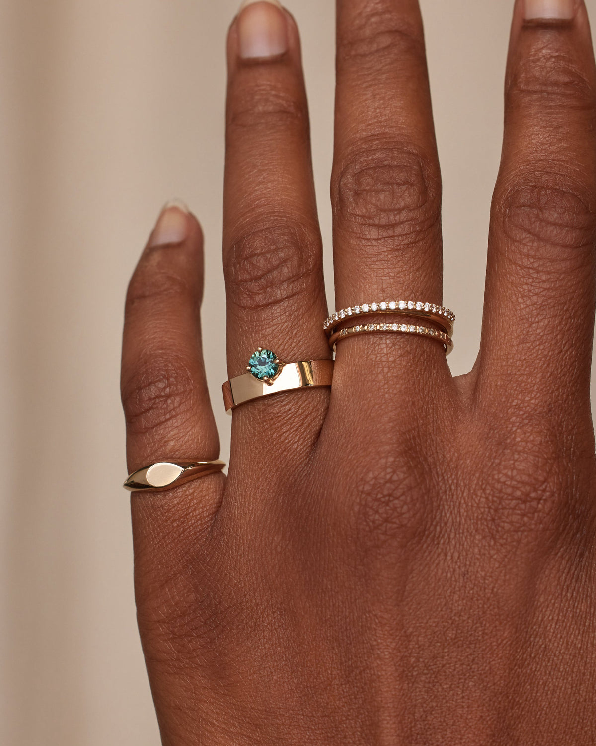 [lifestyle]Hand wearing multiple gold rings with gemstones on a beige background