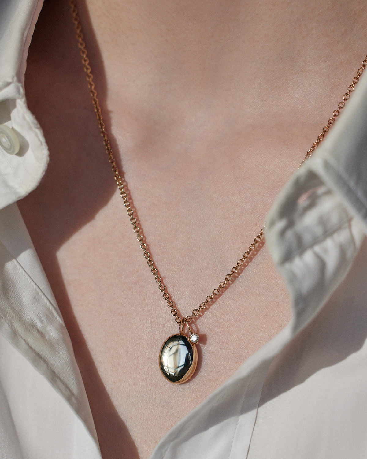 [lifestyle]gold necklace with a pendant on a person wearing a white shirt.