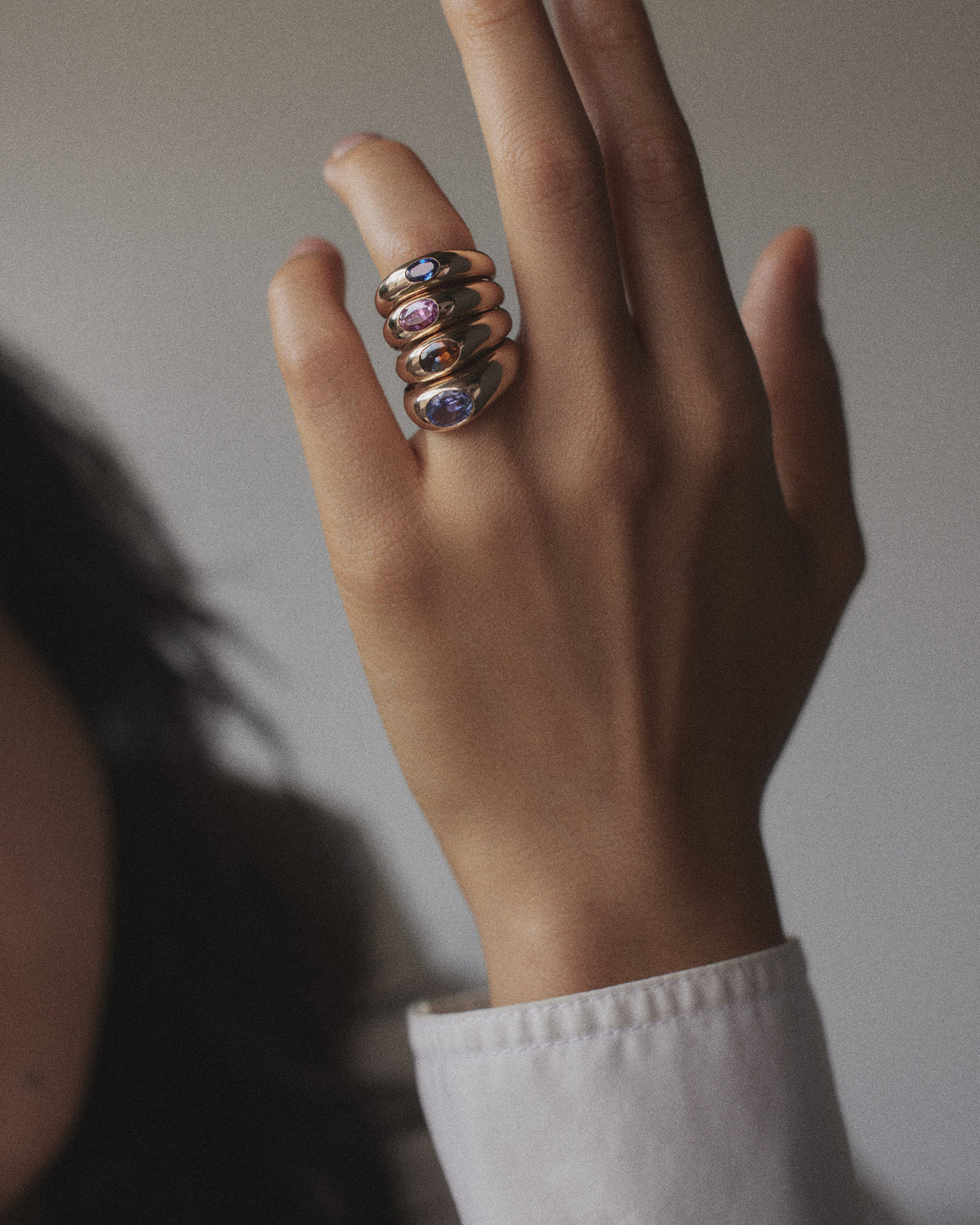 [lifestyle]Hand wearing multiple rings with gemstones on a neutral background