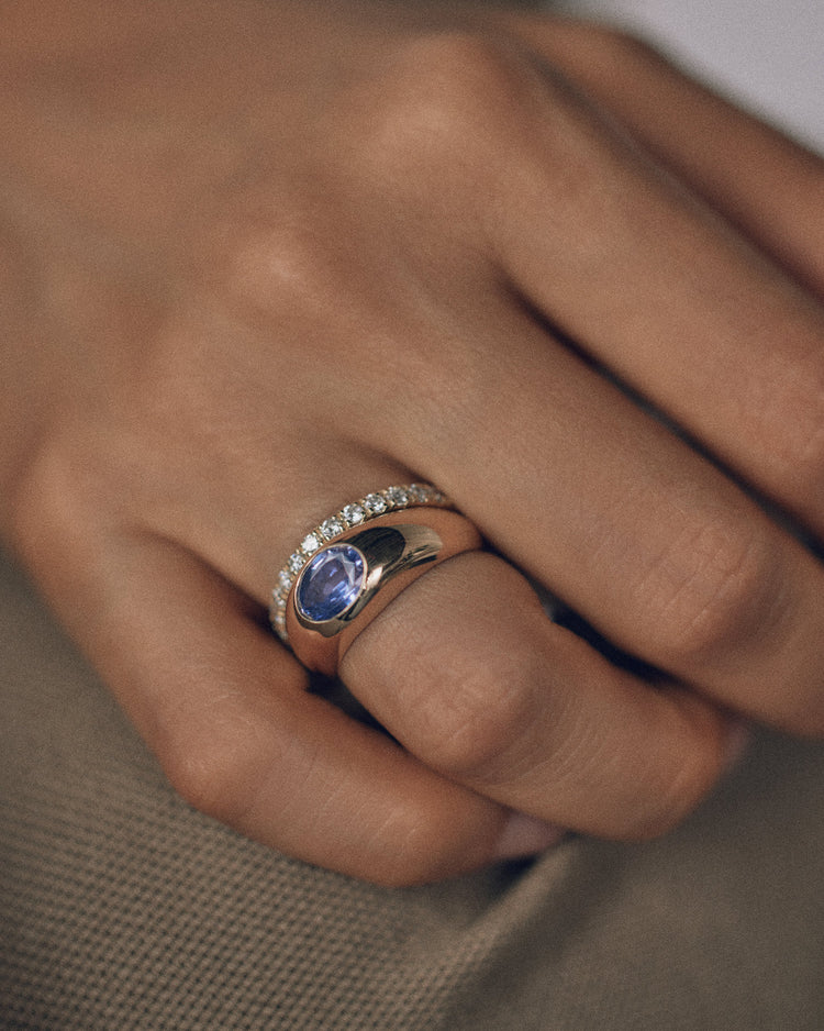 [lifestyle]Close-up of a hand wearing a ring with a blue gemstone on a neutral background