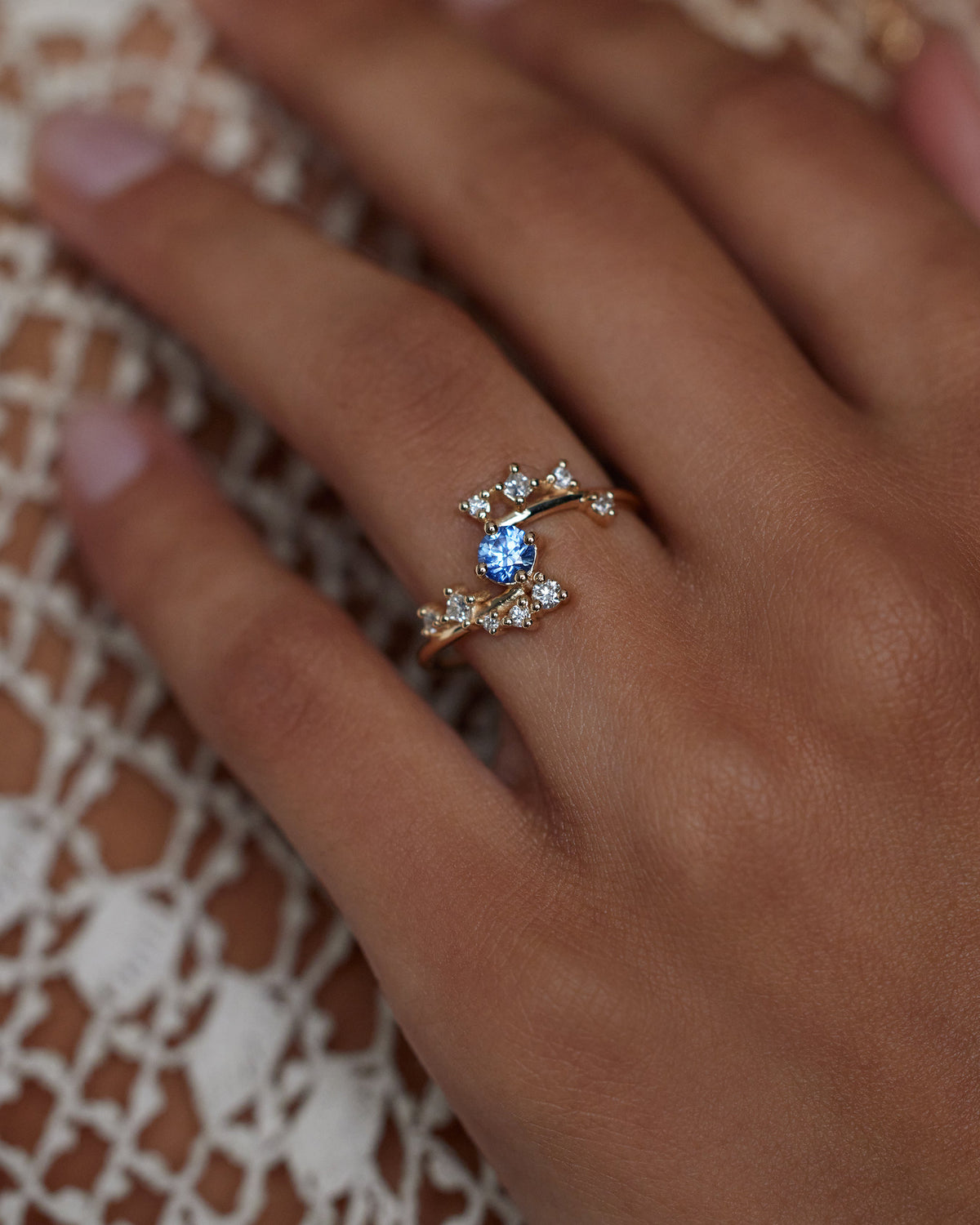 [lifestyle]Close-up of a hand wearing a ring with a blue gemstone on a textured fabric background
