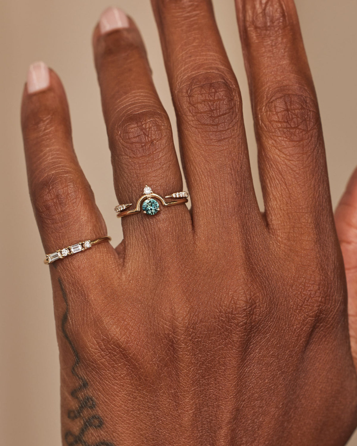 [lifestyle]Hand wearing two rings with a teal stone on a neutral background