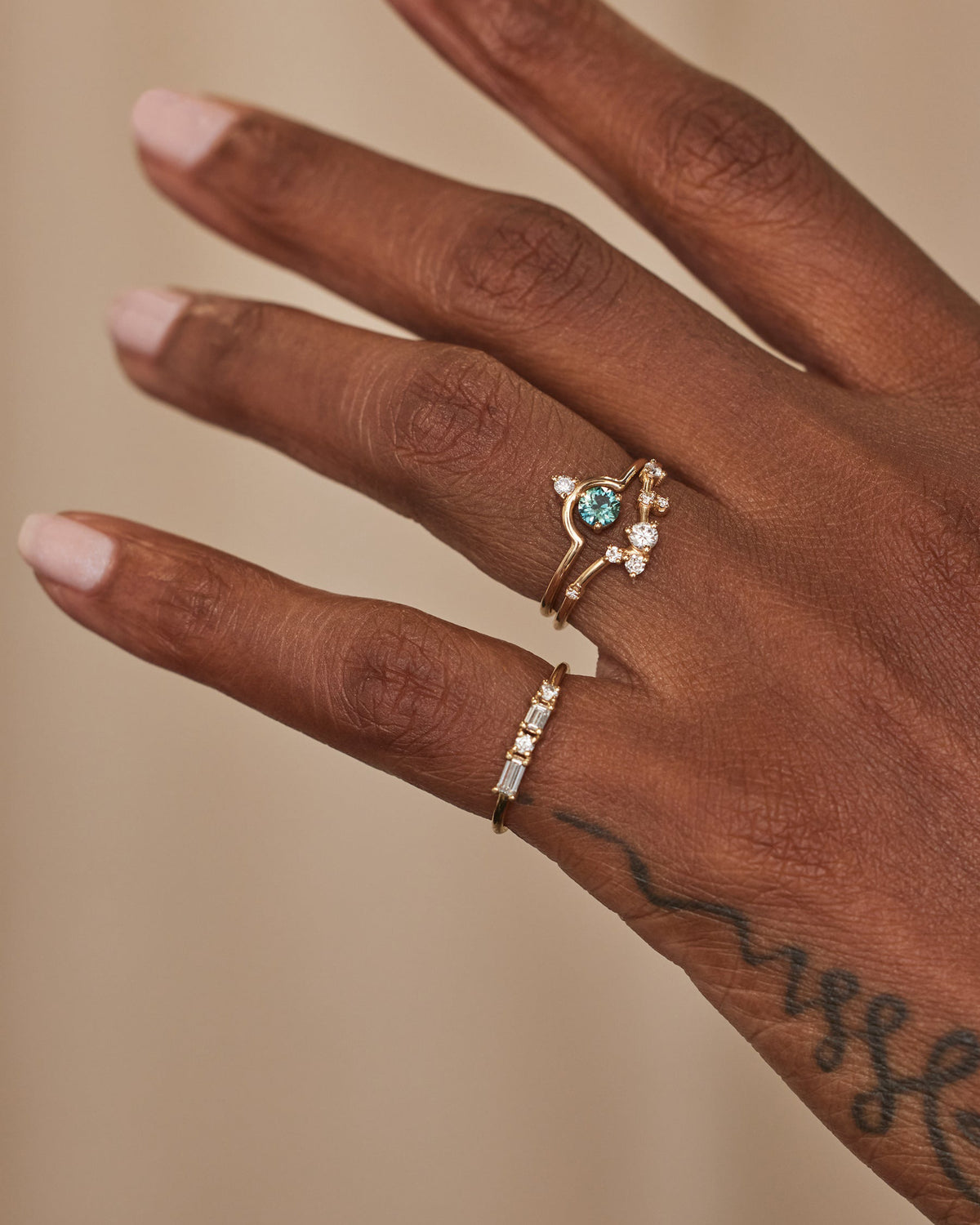 [lifestyle]Hand wearing two gold rings with gemstones on a beige background